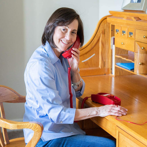 Woman using red corded telephone while sitting at a wooden home office desk